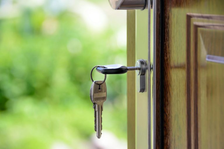Een huis kopen: Stappen die je moet nemen voor de beste deal Key inserted in door lock against a blurred green background, symbolizing security and real estate.