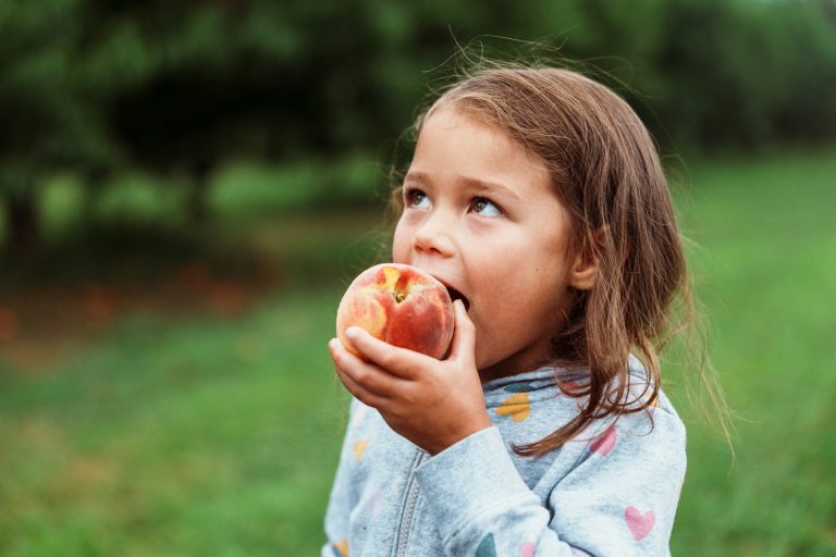 A young girl eating a fresh peach outdoors.